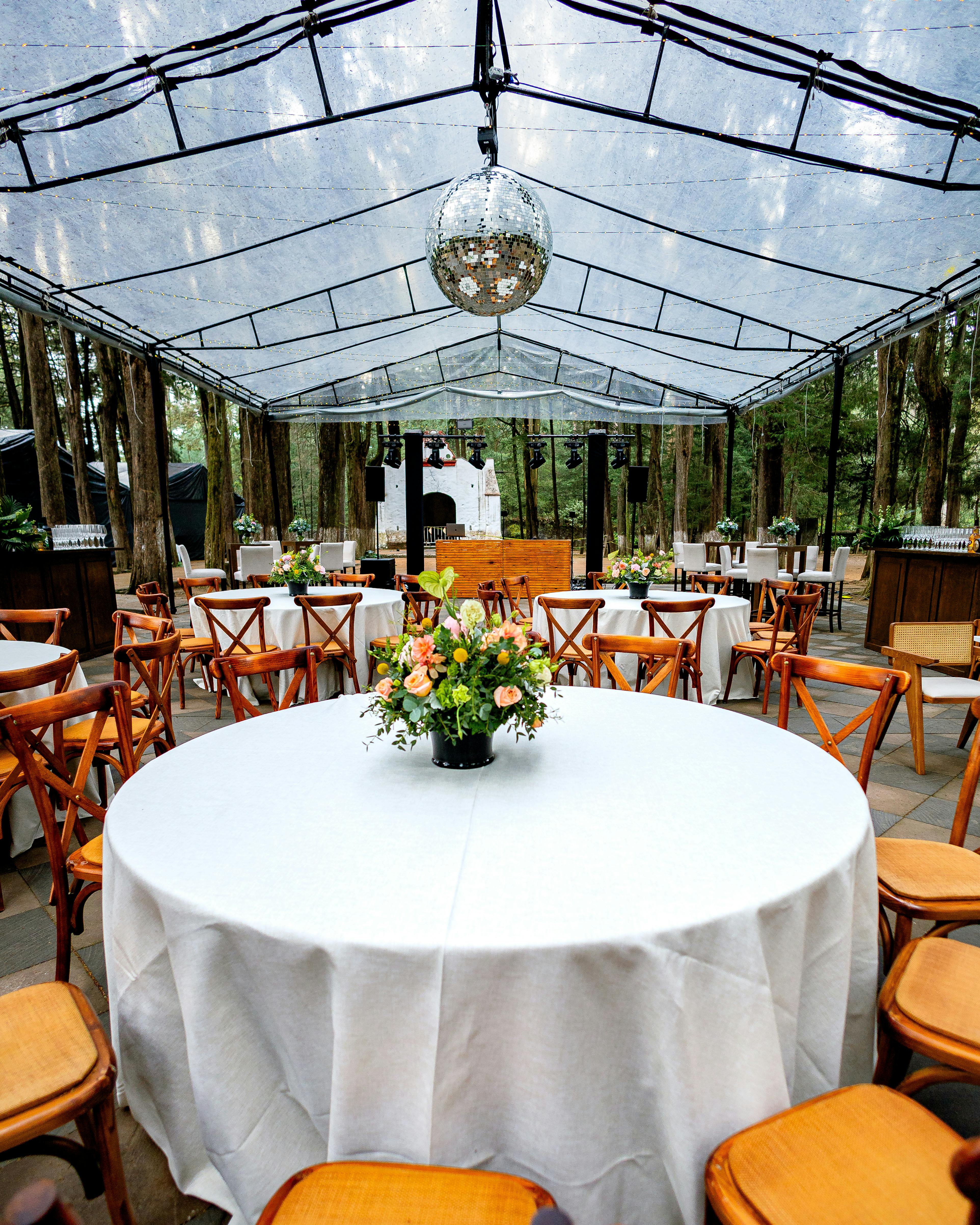 Beautifully decorated outdoor wedding reception under a clear tent with floral arrangements.